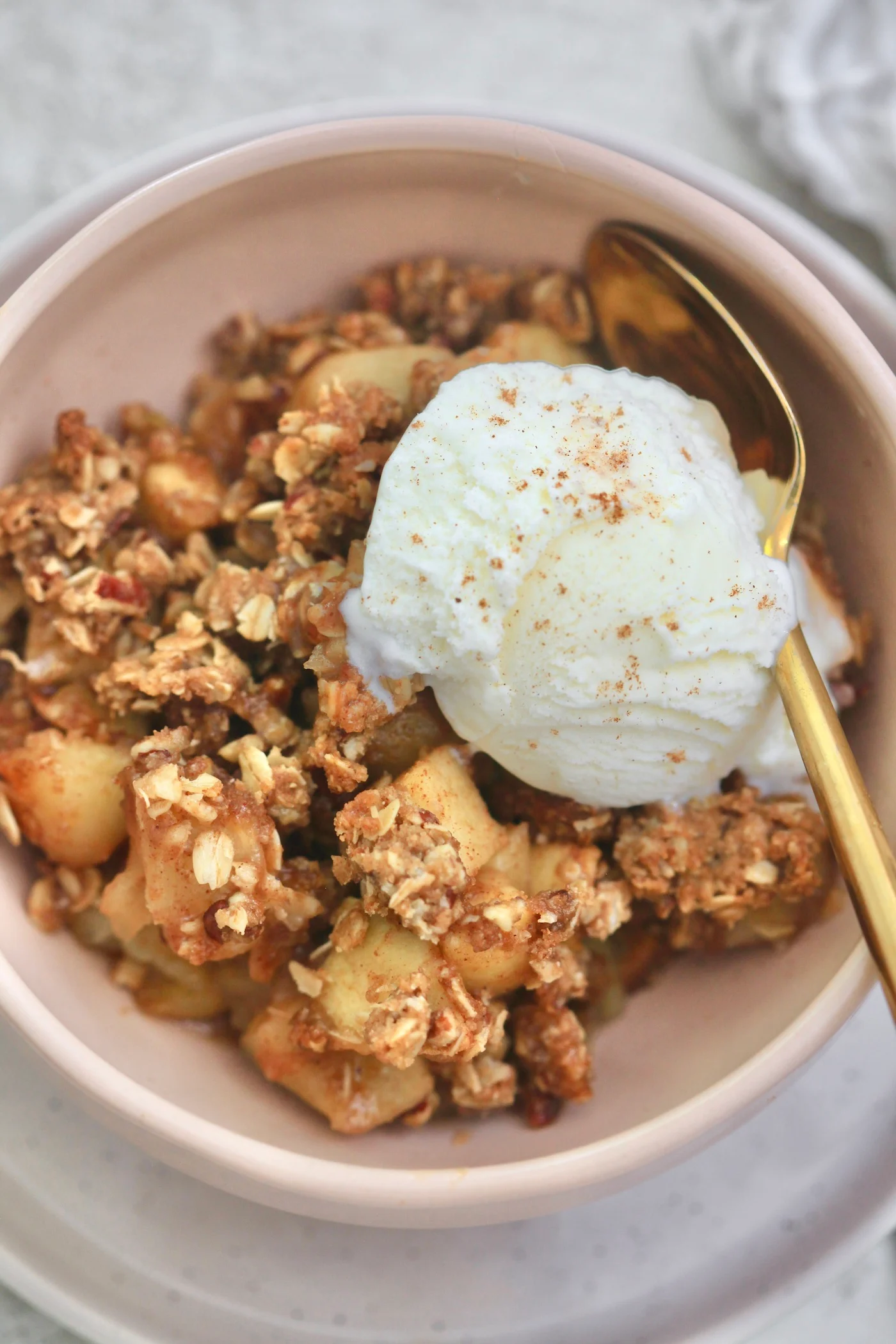 Photo of apple crisp being served in a bowl with a scoop of vanilla ice cream.